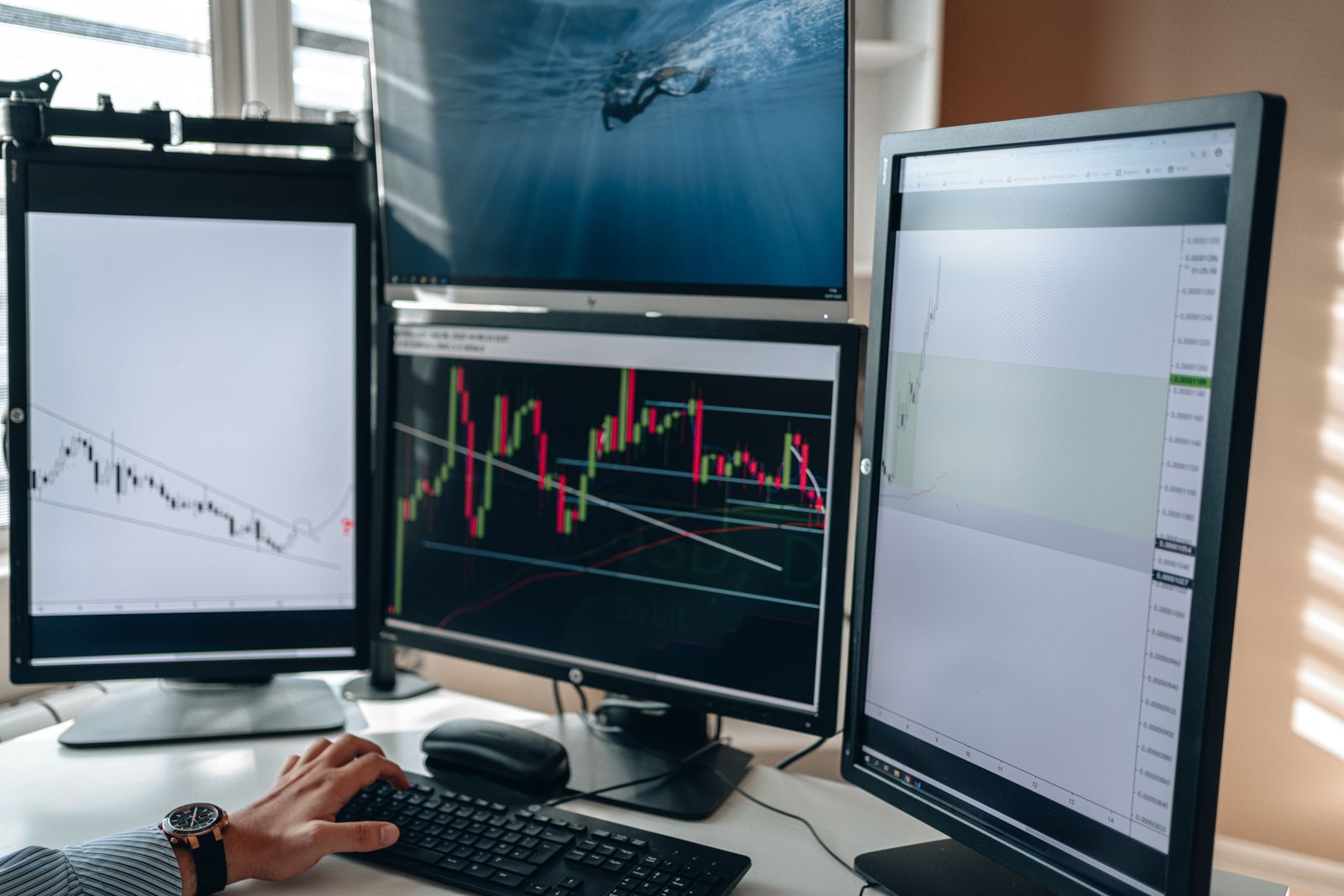 A desk with multiple computer monitors displaying financial charts and market data