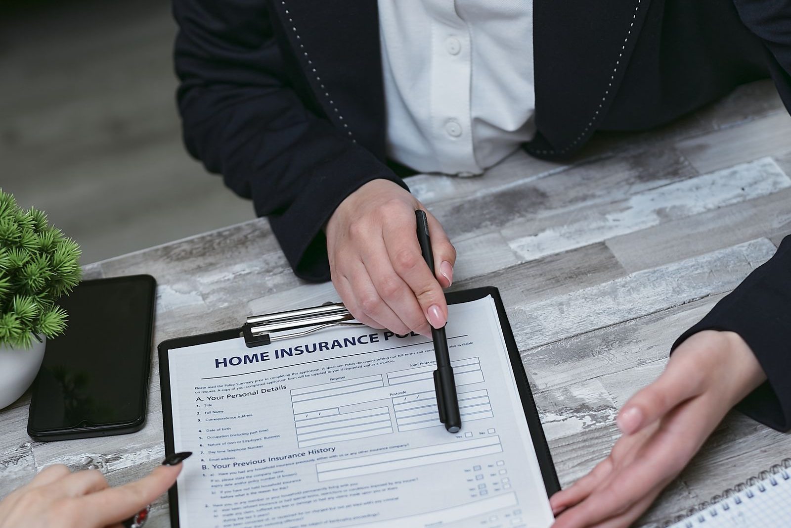 Hands pointing a pen at a home insurance policy document on a clipboard