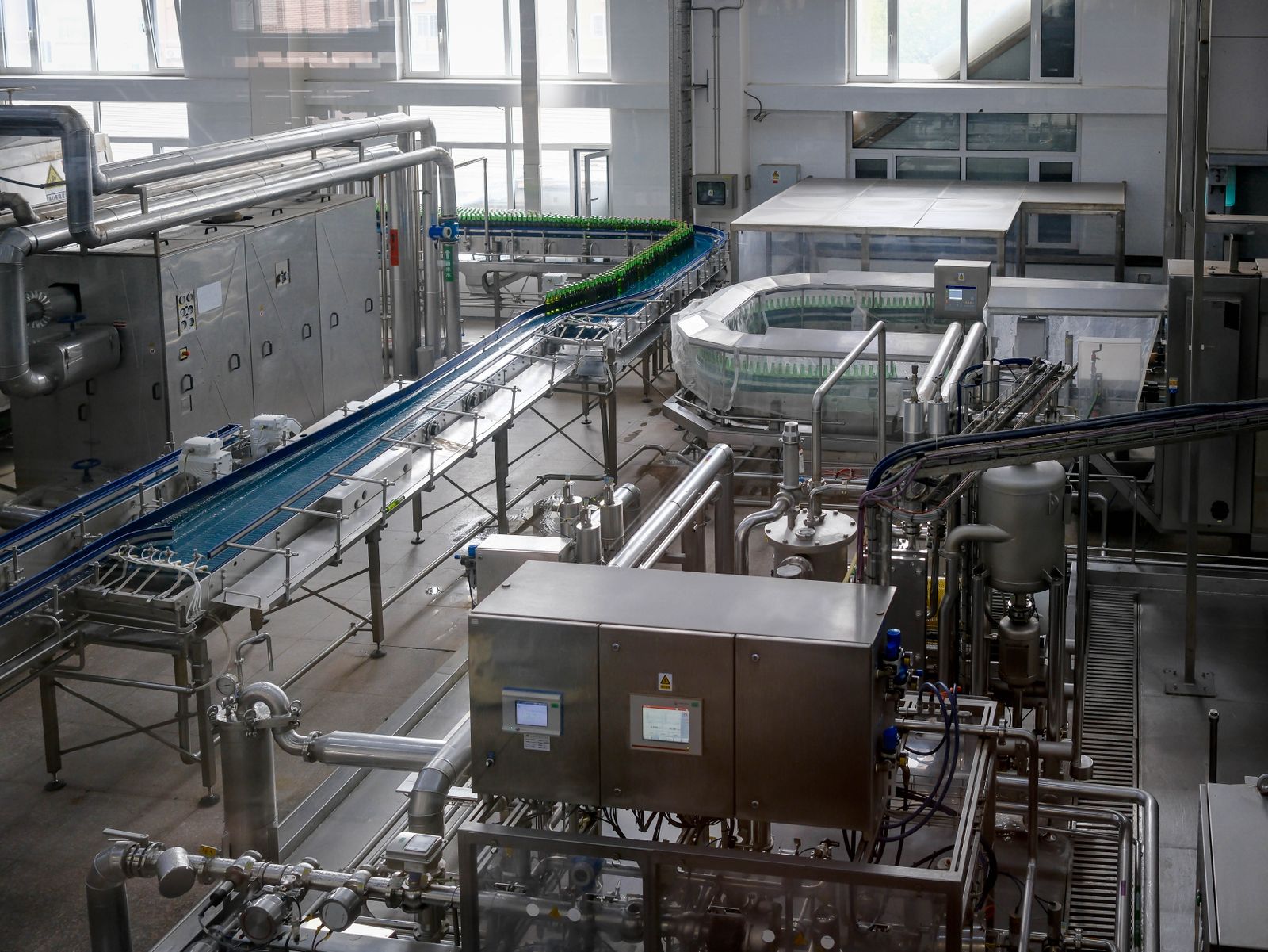 A modern stainless-steel bottling production line with conveyors inside a bright manufacturing plant