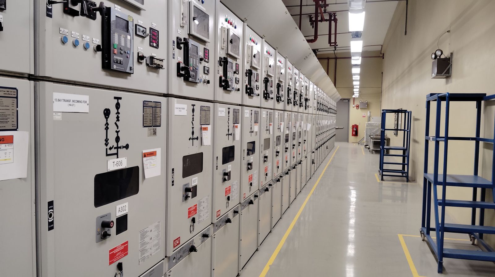 A row of industrial electrical switchgear control panels lining a clean plant equipment room