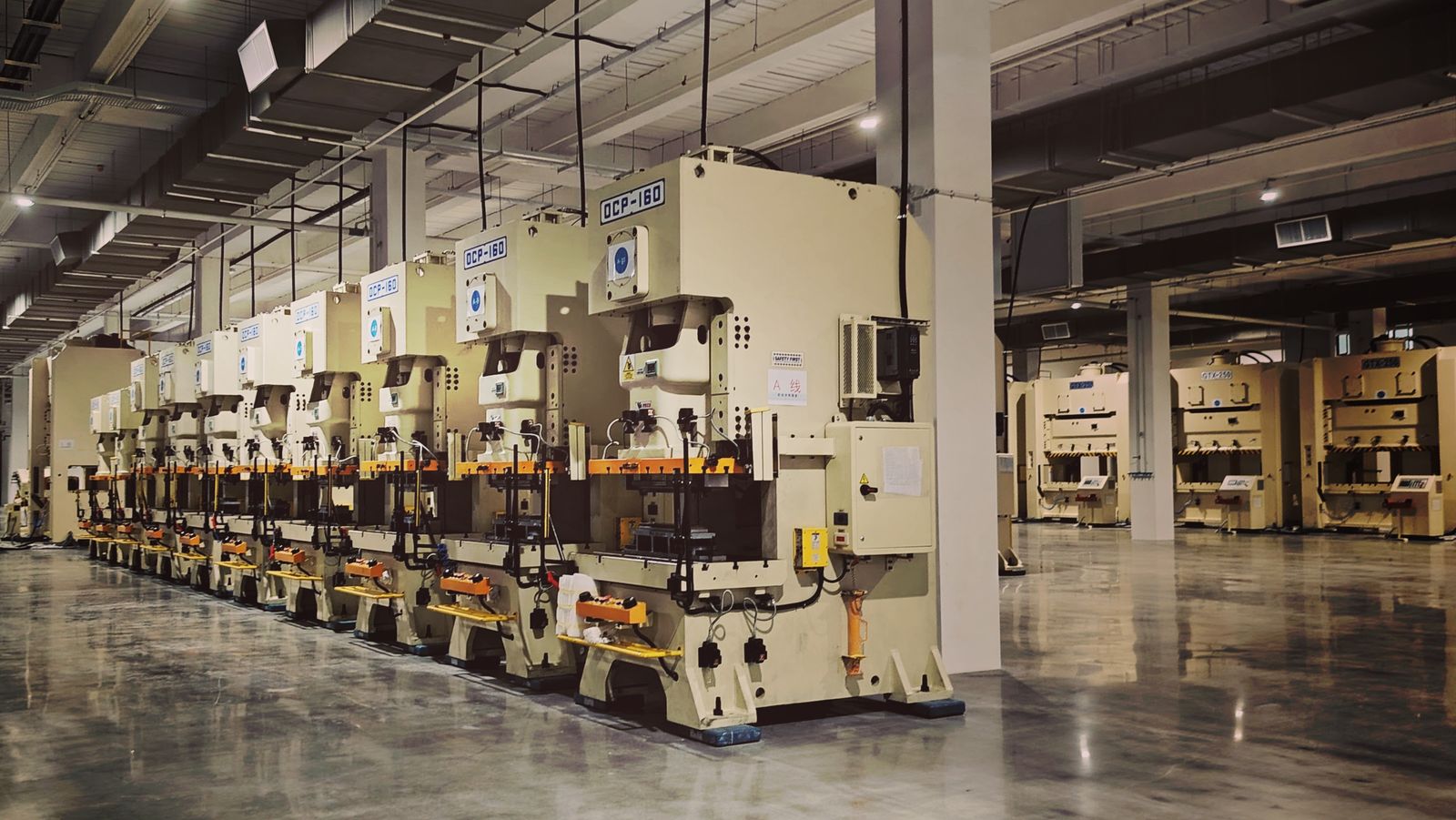 A row of industrial stamping presses on a polished factory floor in a large manufacturing plant