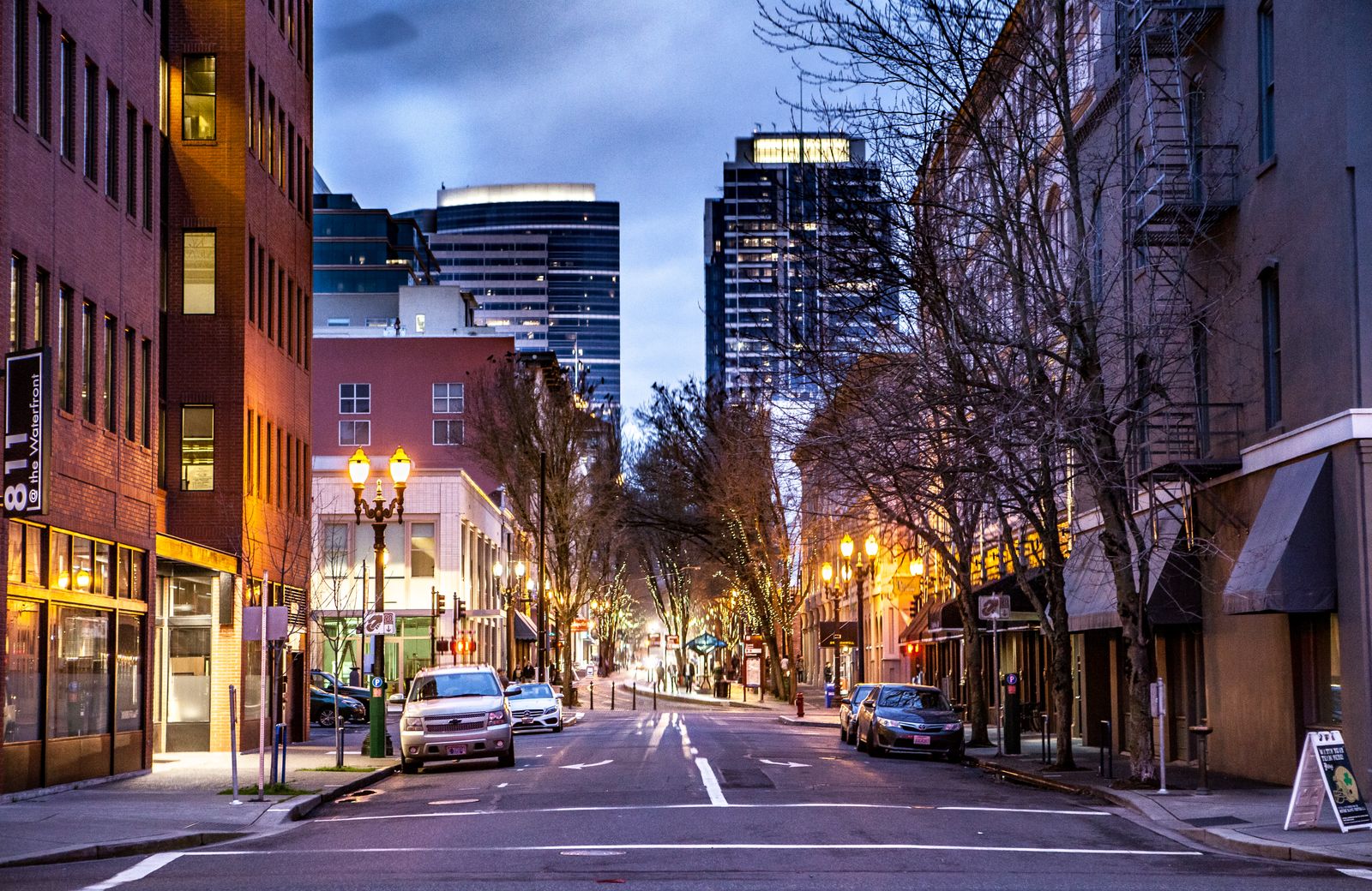 Downtown Portland, Oregon street at dusk with city buildings and tree-lined sidewalks
